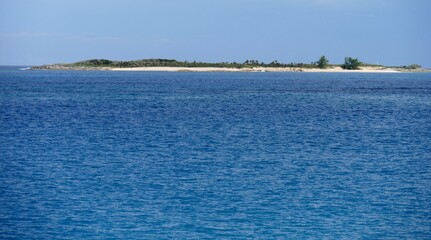 A small island with white sand beach and lush vegetation dots the vast ocean of the Bahamas