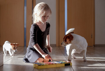 girl playing a xylophone melody sitting on her knees in a gymnastic suit with two jack russell...