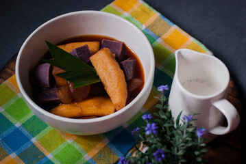 Banana kolak with sweet potato & sugar palm fruits addition on dark grey background. Kolak is an Indonesian dessert based on palm sugar,coconut milk & pandanus leaf. Very popular dish on Ramadan iftar