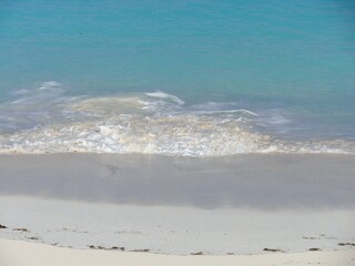 Waves rolling gently against the soft white sand create stunning patterns of foam in a tropical beach