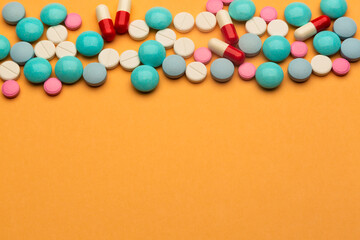 Lot of multicolored pills and tablets on orange background with free space for text or prescription.