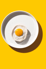 Fried egg on a round plate on a yellow table with hard shadows. The concept of creativity and minimalism in cooking. Top view, flat lay.