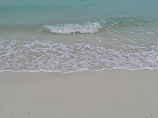 Layers of gentle foaming waves rolling against the fine white sands in a tropical beach