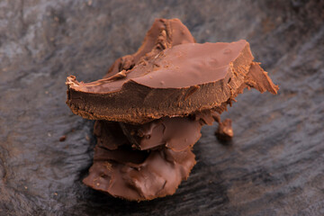 Heap of broken pieces of bitter or milk chocolate scattered on dark background