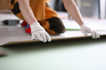 Close-up of adult man installing new laminated wooden floor in room. Professional worker in protective white gloves. Qualified foreman. Construction site concept