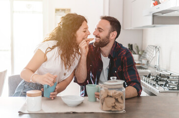 Engaged couple has breakfast together in their new home - young couple jokes while eating cookies -...