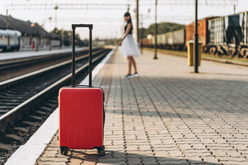 Female brunette traveler with red suitcase walking on raiway station