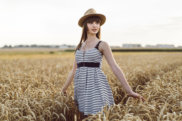 Pretty brunette girl in light dress walking outdoor in wheat field