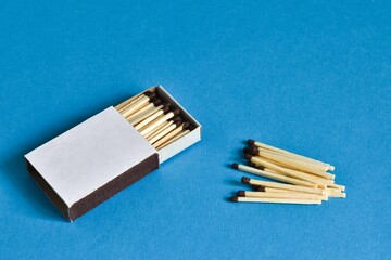A box of matches and nearby matches on a blue background. Place for text