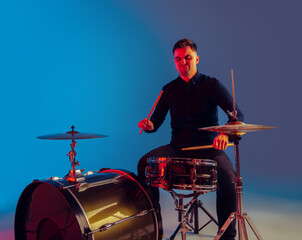 Caucasian male drummer improvising isolated on blue studio background in neon light. Performing,...