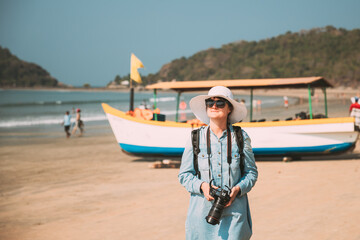 Fototapeta premium Canacona, Goa, India. Young Caucasian Lady Woman With Camera Standing On Famous Palolem Beach Near Arabian Sea In Summer Sunny Day