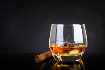 Glass of whiskey and cigar on dark background.