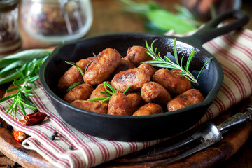 Grilled mini sausages or bangers in a cast iron skillet with fresh rosemary sprigs - obrazy, fototapety, plakaty
