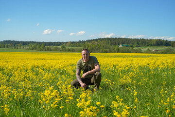 Fototapeta na wymiar a white man sits on a large field with yellow flowers near the forest, and blue sky