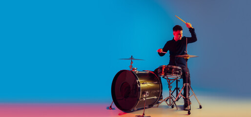 Caucasian male drummer improvising isolated on blue studio background in neon light. Performing,...