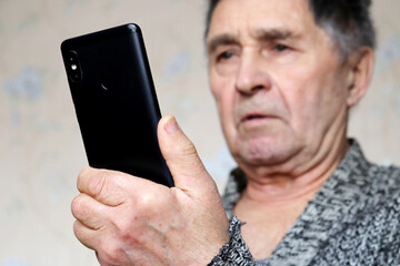 Elderly man with mobile phone looking surprised on smartphone display. Concept of online communication in retirement, sms, social media and news