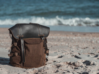 Hipster hiker tourister khaki backpack close up on background blue sea ocean horizon on sand beach, blurred panoramic seascape blank, traveler relax holiday concept, sunlight view in trip vacation