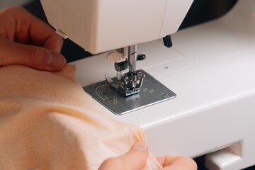 The seamstress inserts the cloth under the sewing machine for the overlock. A closeup view of...