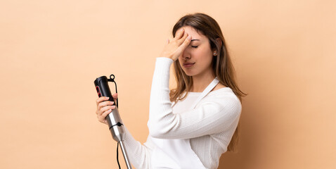 Woman using hand blender over isolated background with headache