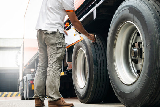 Truck driver holding clipboard daily check safety a truck wheels and tires.