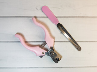 Grooming scissors with pink handles and emery board for pet on a light wooden background. Grooming tools for the hygienic care of pets cats and dogs. - obrazy, fototapety, plakaty