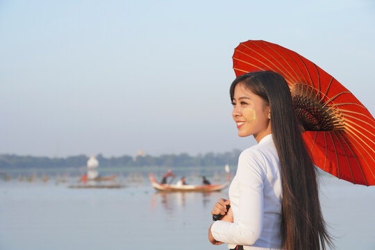 A beautiful Myanmar woman with traditional dress and holding red umbrella standing near the lake ,U-beng bridge,Mandalay Myanmar.