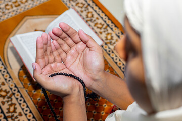 Muslim Asian women raise their hands to pray on the mat at home. Indoors. Focus on hands.