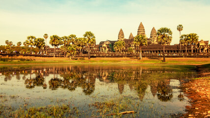 Fototapeta na wymiar Ruins of Khmer temple Angkor Wat with reflection in lake, water. Main gate to Angkor Wat with palm trees, stone road. Landscape background. Author's space. Large space for an inscription or logo