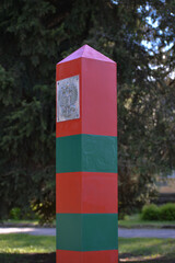 Red-green border post with the Russian coat of arms on the background of a green tree. Russian border. Border troops