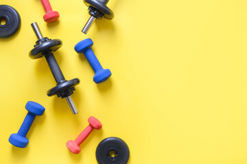 Sport colorful dumbbells on yellow background. Top view, copy space.