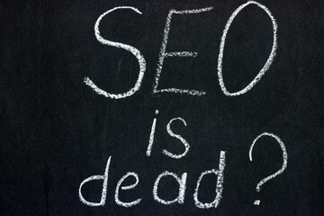 
The phrase "SEO is dead?" on a dark background chalk boards. An important issue for the younger generation of copywriters