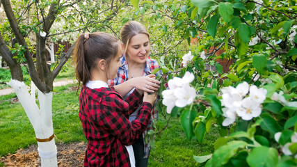 Obraz premium Portrait of young mother with teenage daughter working in garden and taking care of trees