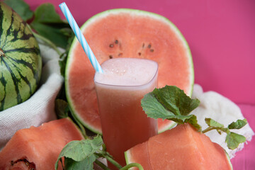 Glass of watermelon juice and fruits (Citrullus lanatus) on pink background