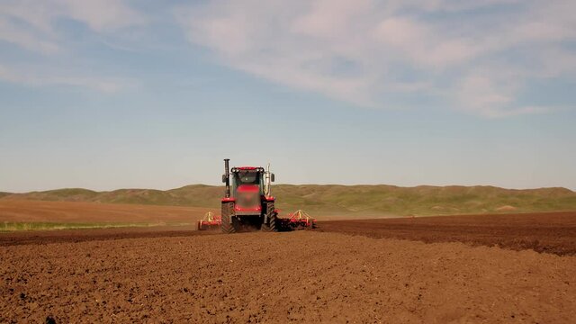 A red combine harvester is moving towards the operator. A combine harvester plows fields and drives towards the camera, against the background of a mountain