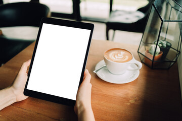 A woman hands are holding a mockup of black tablet with blank white screen in the cafe with a white...