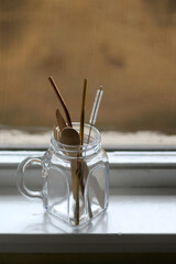 Wooden cutlery and reusable metal straws in a glass jar. Selective focus.
