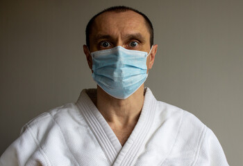 A young strong man in a white kimono for sambo, jiu jitsu and other martial arts with a blue medical gloves and medical mask.