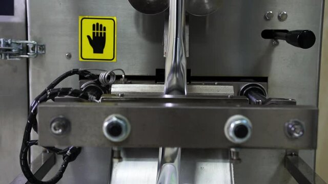 Close-up of the working process of a technical, metal device that creates food sachets of silver color at the enterprise for packaging products.