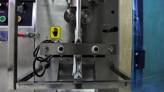 Work process at the enterprise, metal, technically equipped device which packs by means of the heated Press small, silver-colored sticks and fills in them various foodstuff, close-up