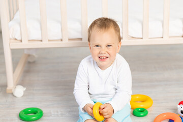 portrait of a smiling child playing near the crib, baby boy 2 years old sitting with toys, early development