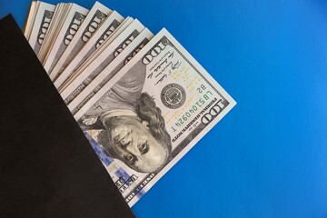Several hundred-dollar bills are in a black envelope. The problem of the shadow economy. Blue background. Free space for text