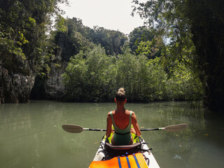 A girl is swimming in a sea kayak and rowing oars in the background of mountains