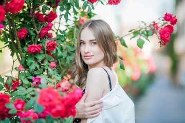 Young beautiful woman walks in a European city. Portrait of a young woman near blooming roses. Europe.