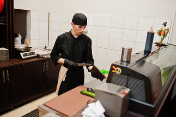 Professional chef wear in black making sushi and rolls in a restaurant kitchen of japanese traditional food.