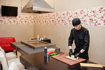 Professional chef wear in black making sushi and rolls in a restaurant kitchen of japanese traditional food.