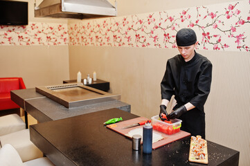 Professional chef wear in black making sushi and rolls in a restaurant kitchen of japanese traditional food.