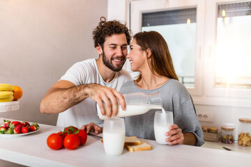 Young cheerful couple having fun during breakfast time in the kitchen. Cheerful young man hugging...