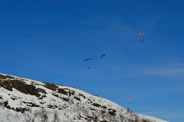 Naklejka na ściany i meble paragliders on vibrant blue sky over snowy mountain