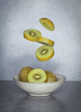 kiwi gold en rodajas faltando cayendo sobre un bol con mas kiwis