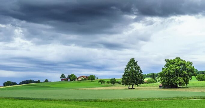 Timelapse de nuages noirs mena&ccedil;ants au-dessus d'un champ de culture avec une ferme et des plantations en suisse romande